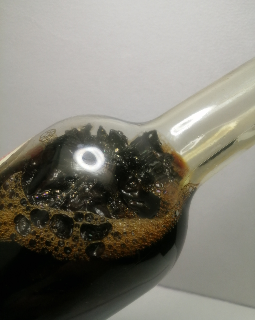 A close-up of a clear glass bottle containing 8week cold macerated black walnut husk, photographed against a plain light background.