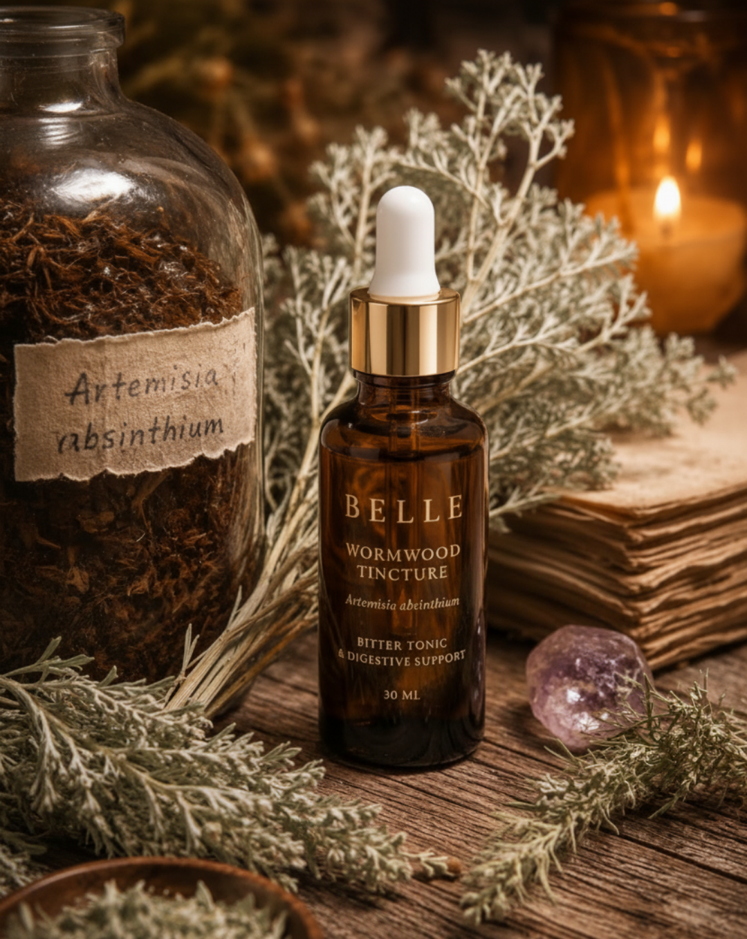 Belle Wormwood Tincture amber glass dropper bottle on a rustic wooden surface, surrounded by dried herbs, a crystal ball, an old book, and a lit candle in the background.