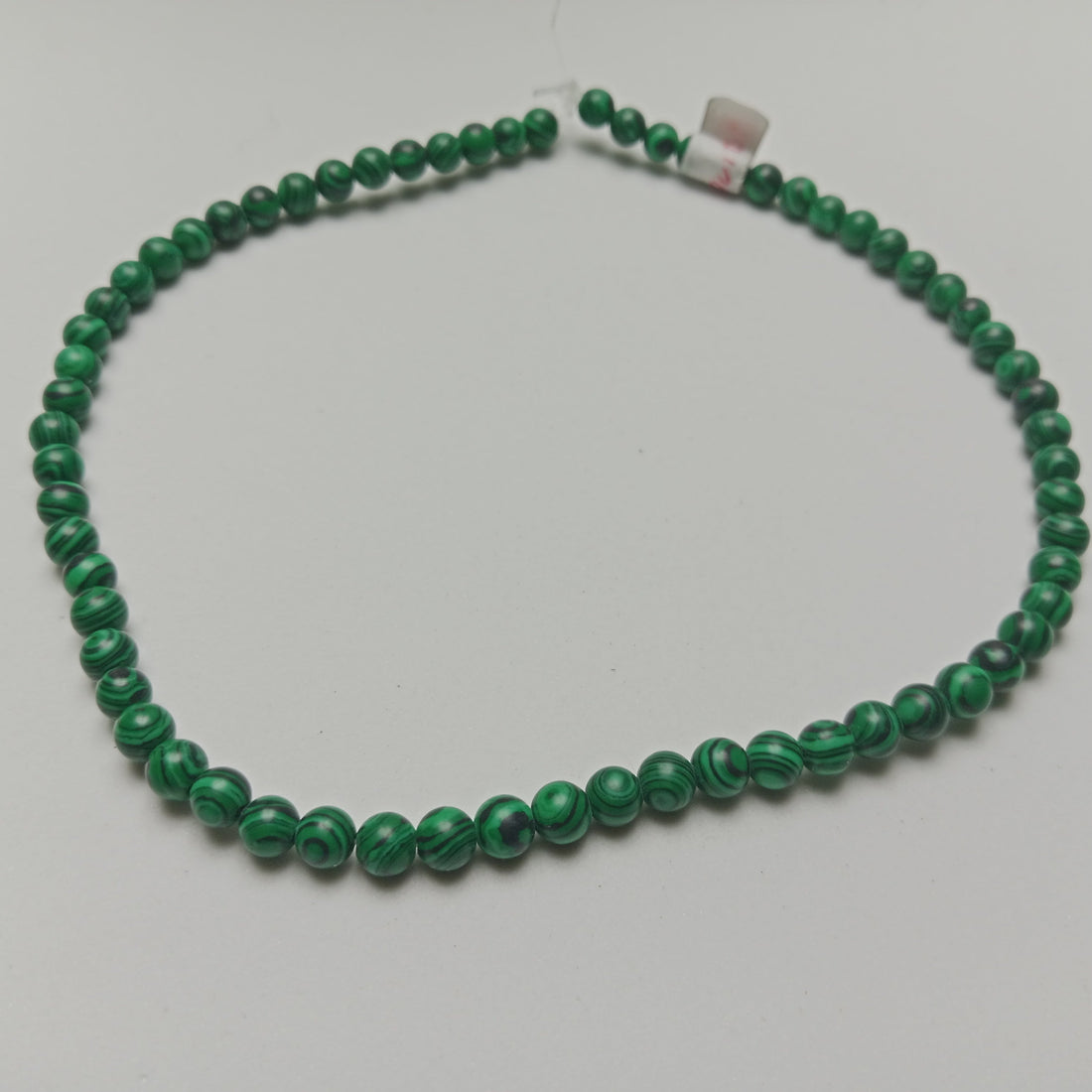 High-resolution macro photograph of polished Malachite beads showing rich emerald green layers and complex circular swirls, arranged beautifully on a dark slate background at Belle Atelier.