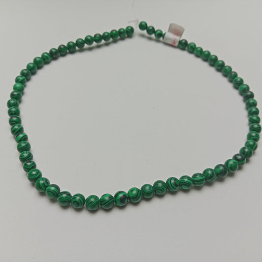 High-resolution macro photograph of polished Malachite beads showing rich emerald green layers and complex circular swirls, arranged beautifully on a dark slate background at Belle Atelier.