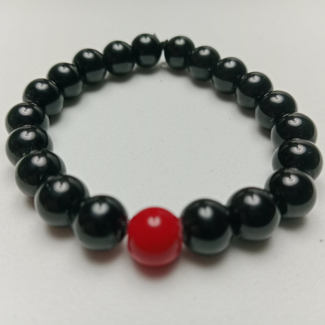 Sleek studio photograph of highly reflective, polished Black Obsidian beads showcasing a glossy volcanic glass finish, hand-arranged on a dark minimal concrete block at Belle Atelier.