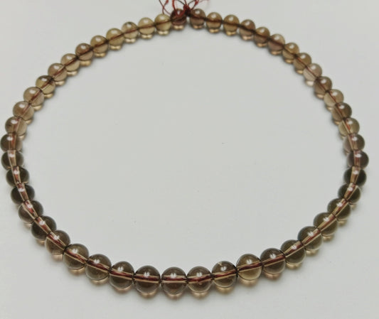 Macro studio photograph of translucent deep tea-brown and charcoal gray 6mm Smokey Quartz gemstone beads hand-assembled on a minimalist slate gray surface at Belle Atelier.