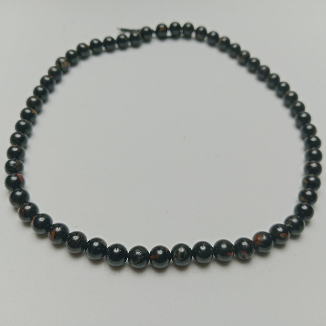 Studio photograph of raw Black Tourmaline crystals with visible natural ridges, styled symmetrically next to hand-assembled protection jewelry on a matte black stone surface at Belle Atelier.