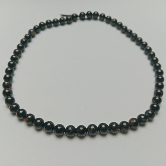Studio photograph of raw Black Tourmaline crystals with visible natural ridges, styled symmetrically next to hand-assembled protection jewelry on a matte black stone surface at Belle Atelier.