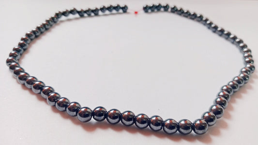 High-contrast studio photograph of heavy, metallic-luster Hematite beads displaying deep iron-black sheen, organized on a raw gray slate tile at Belle Atelier.