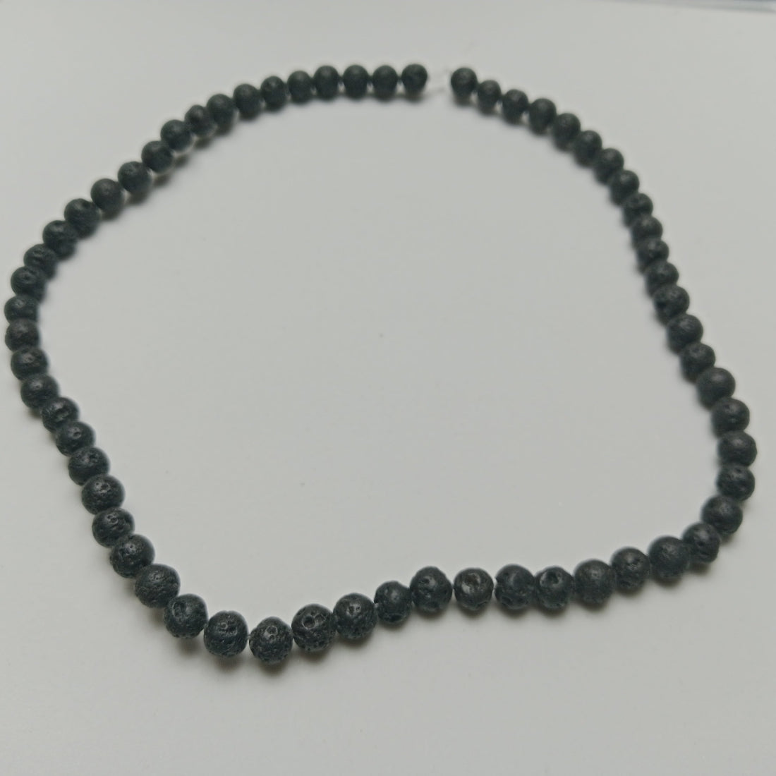 Macro view of black, porous, calibrated 6mm Lava Stone volcanic rock beads on a natural linen cloth background at Belle Atelier workspace.