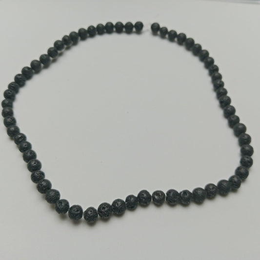 Macro view of black, porous, calibrated 6mm Lava Stone volcanic rock beads on a natural linen cloth background at Belle Atelier workspace.