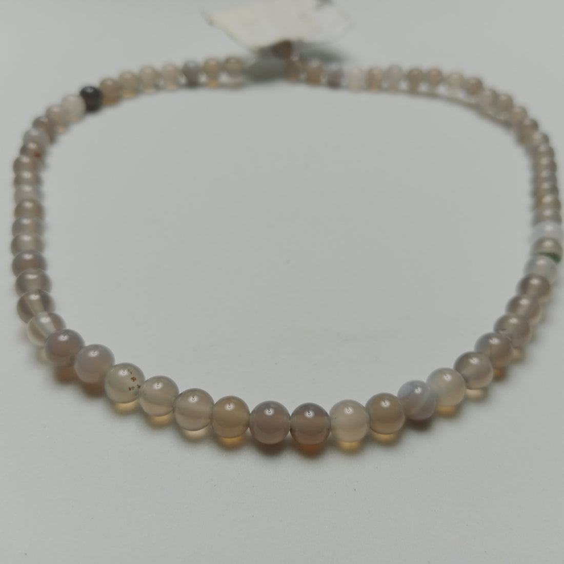 Macro studio photograph of a calibrated layered Gray Agate gemstone strand showing subtle white bands and cloudy gray textures, styled on a neutral stone slab at Belle Atelier.