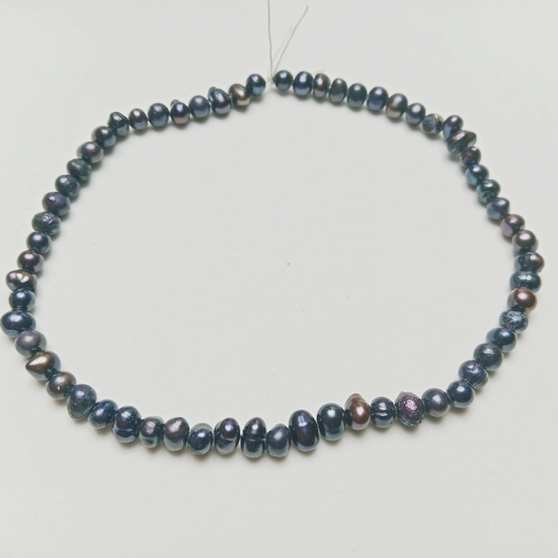 Studio photograph of dark iridescent Black Pearls displaying elegant organic shimmering surfaces, arranged on a soft, minimalist architectural concrete platform at Belle Atelier.