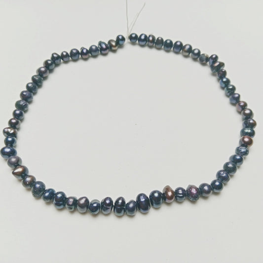 Studio photograph of dark iridescent Black Pearls displaying elegant organic shimmering surfaces, arranged on a soft, minimalist architectural concrete platform at Belle Atelier.