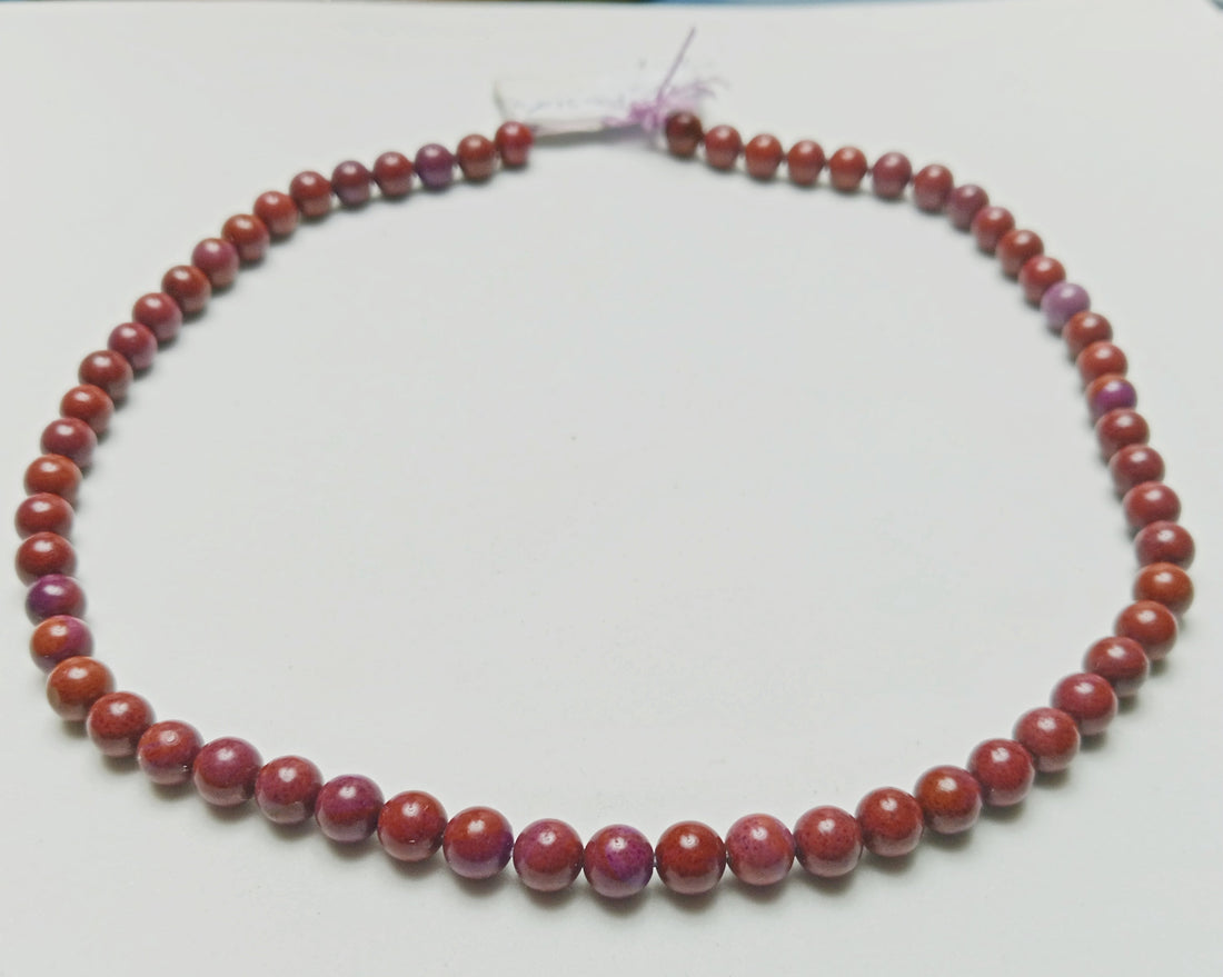 Studio photograph of opaque, deep terracotta Red Jasper beads showing solid, earth-toned textures, hand-assembled as protection jewelry on a raw concrete surface at Belle Atelier.
