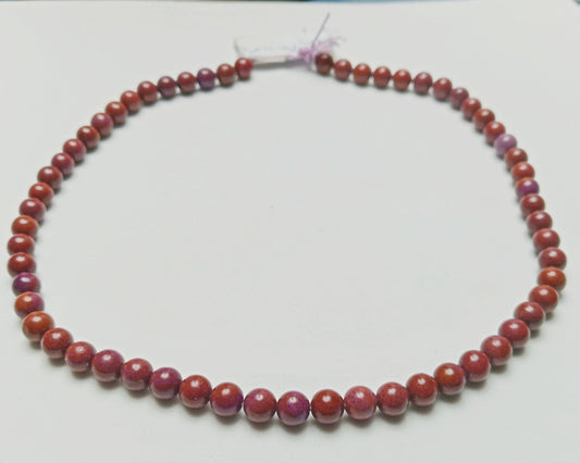 Studio photograph of opaque, deep terracotta Red Jasper beads showing solid, earth-toned textures, hand-assembled as protection jewelry on a raw concrete surface at Belle Atelier.