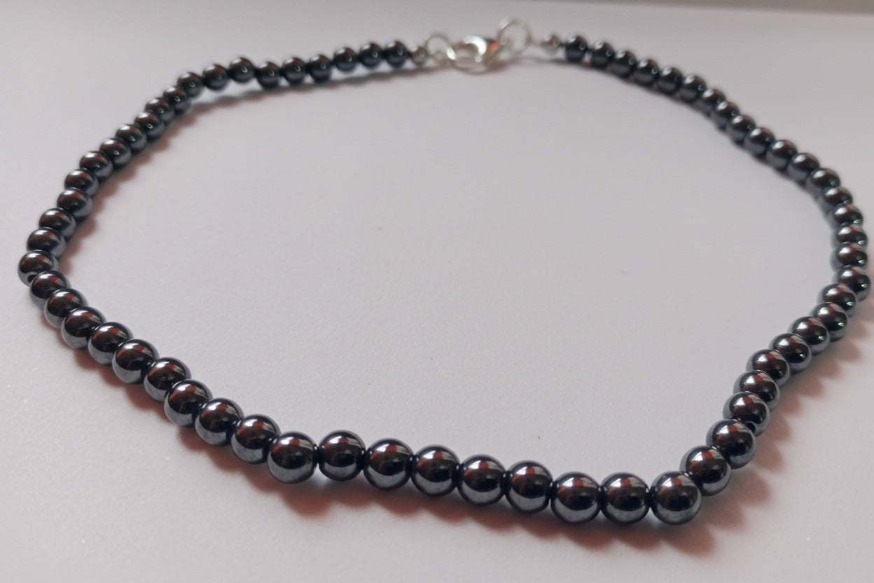 An overhead product shot of a finished 6mm polished black hematite bead necklace displaying a high metallic luster and a secure clasp closure.
