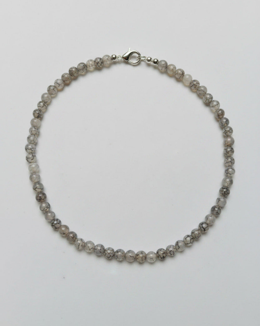 Top-down minimalist studio photograph of a hand-assembled Veined Dragon Agate protection bracelet with distinct matrix lines, resting on a clean black concrete block at Belle Atelier.