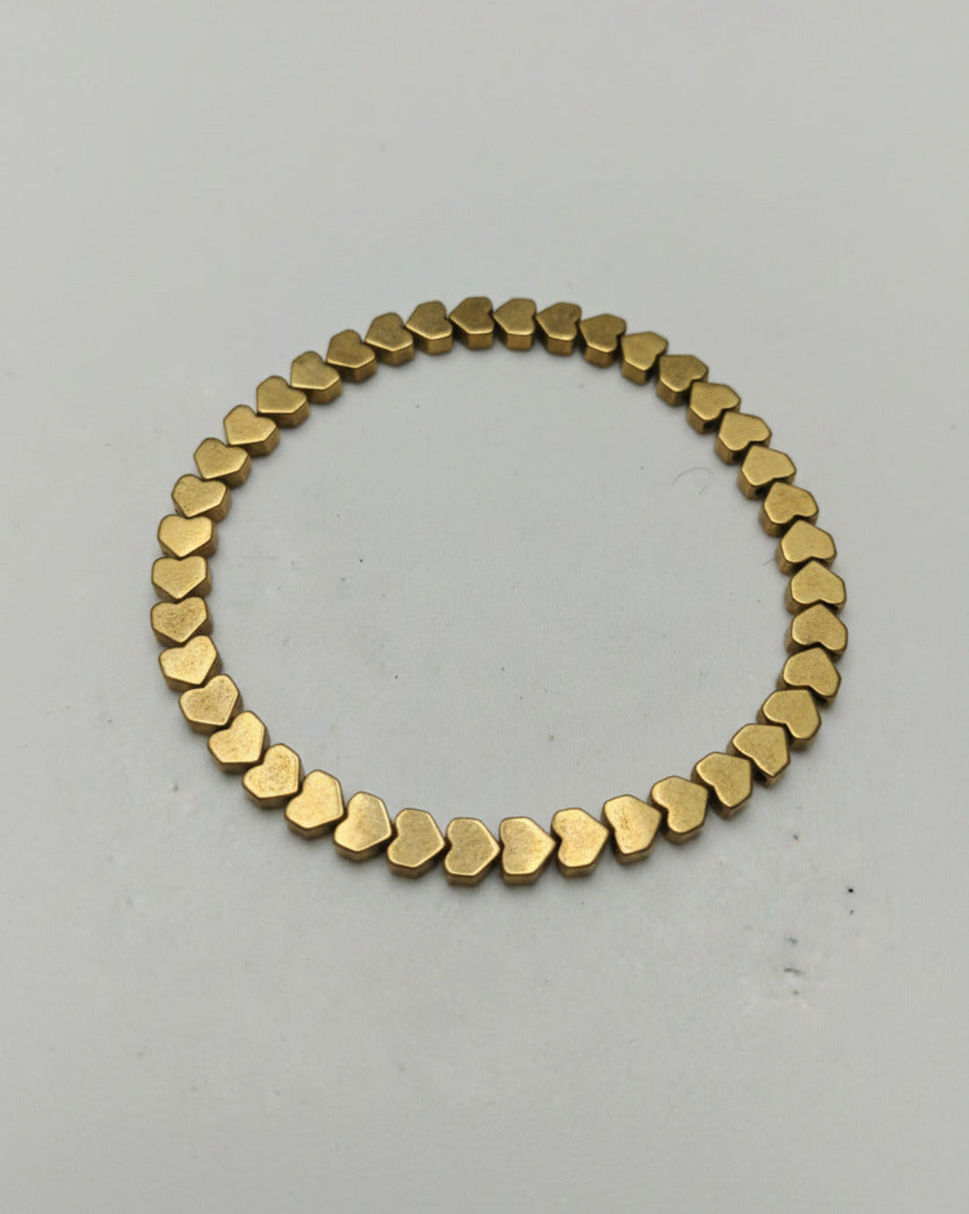 A flat lay view of a gold tone hematite heart shaped bead bracelet strand arranged elegantly on a clean background.
