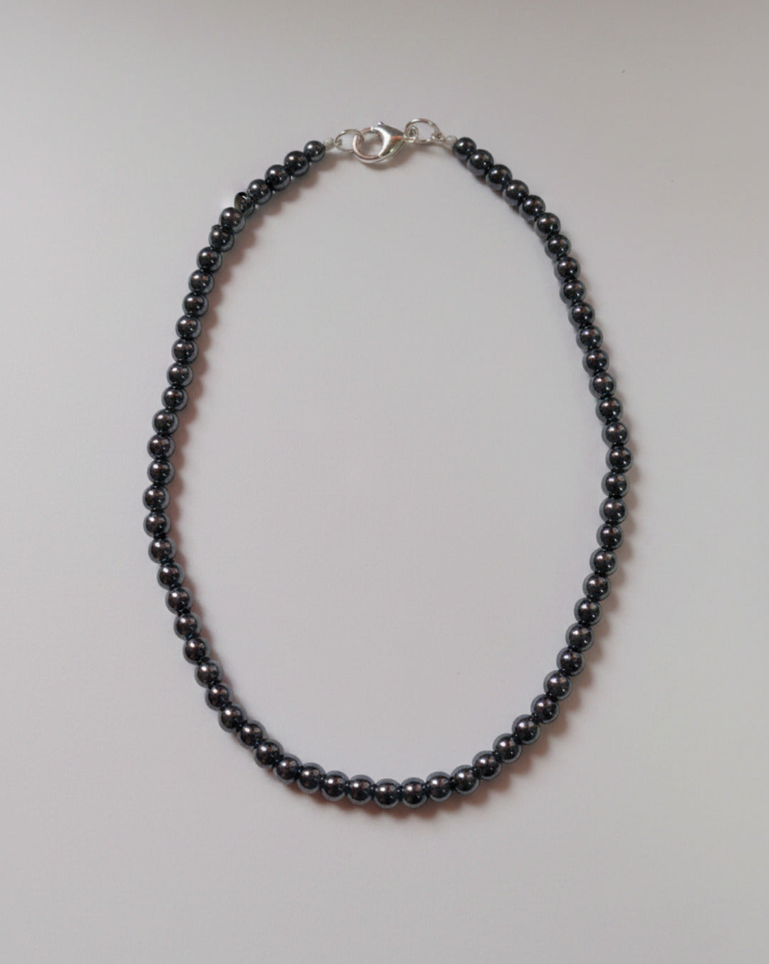 An overhead product shot of a finished 6mm polished black hematite bead necklace displaying a high metallic luster and a secure clasp closure.
