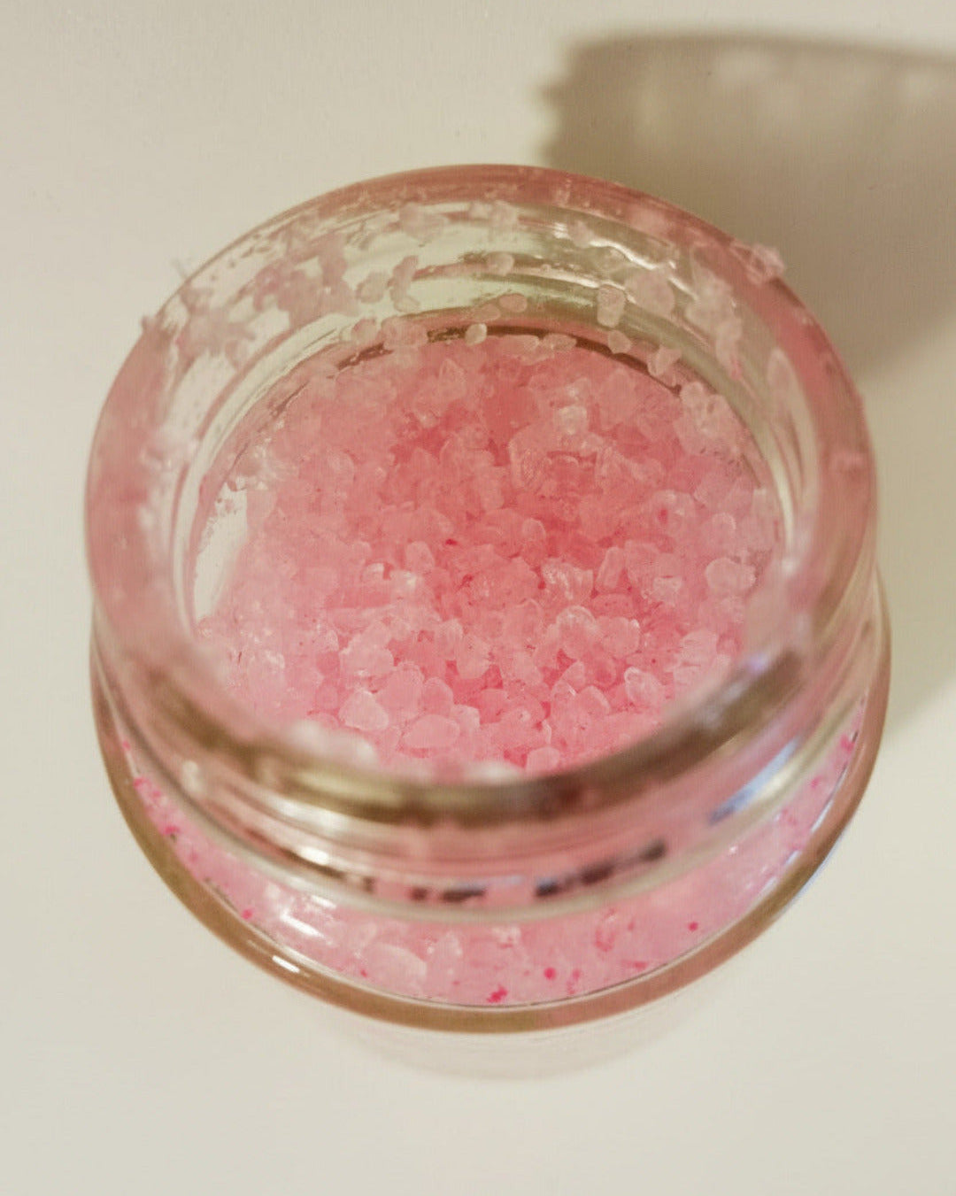 Pink crystal bath salts in a clear glass jar, viewed from above.
